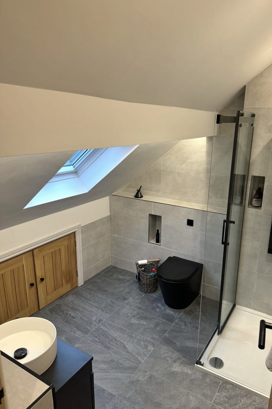 Loft bathroom with grey stone-effect tiles, a black wall-hung toilet and black-framed shower
