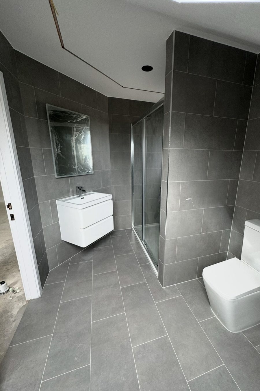 Grey-tiled bathroom with a wall-hung vanity, shower enclosure and toilet